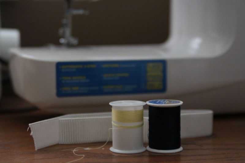 Yellow and dark blue thread and elastic in front of a sewing machine
