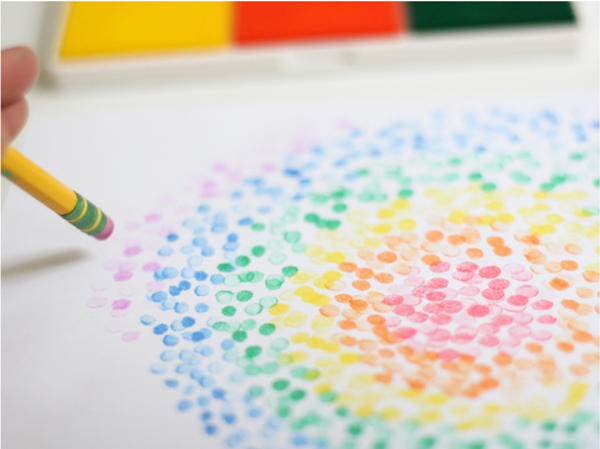 Pencil eraser being used to stamp colored circles on a piece of paper
