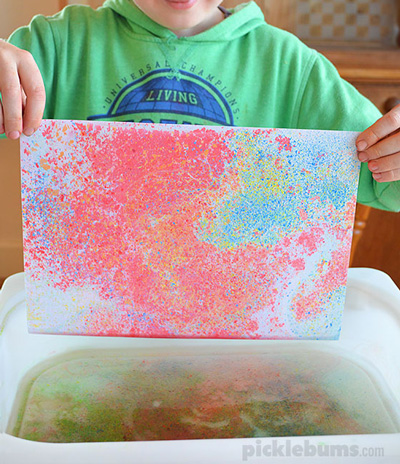 Boy pulling paper with marbled design from tub of water