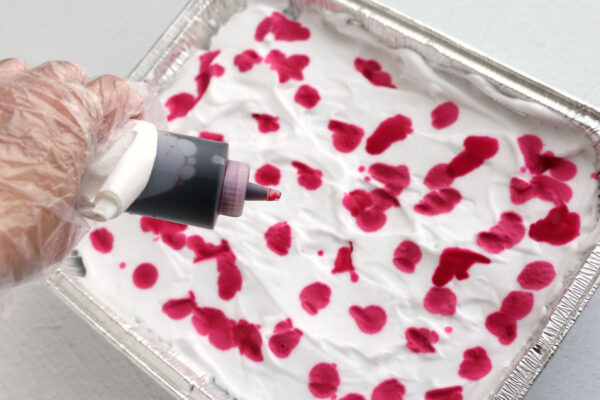 Dripping dots of dye onto the shaving cream.